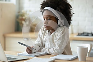 Close up African American little girl wearing headphones watching webinar