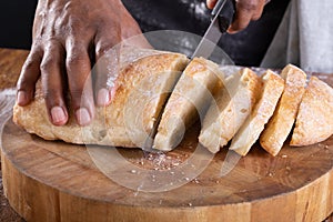 Close-up of african american male baker slicing bread on wooden cutting board