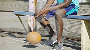 Close-up of African American male sitting on the bench and playing ball, sadness
