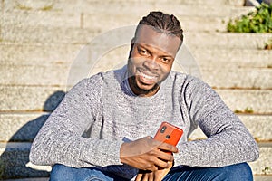 Close-up of African American man sitting on stairs smiling, looking at camera, on a sunny day. Happy young Latino man