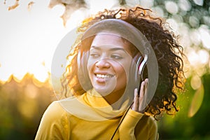 Close-up of african american woman listening to music with headphones outdoors. Young girl with curly hairstyle in