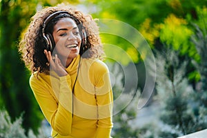 Close-up of african american woman listening to music with headphones outdoors. Young girl with curly hairstyle in