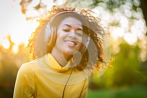 Close-up of african american woman listening to music with headphones outdoors. Young girl with curly hairstyle in