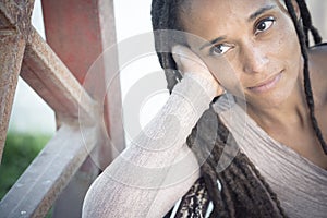 Close up of african american woman with long braided hairstyle resting face on palm of her hand and looking away outdoors.