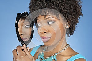 Close-up of African American woman looking at herself in mirror over colored background