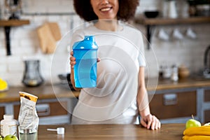 Close-up of african american woman in sports clothing holding shaker with protein cocktail at the kitchen selective focus