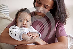 Close up of African American  young young adult mother holding her baby boy in her arms, as he looks to camera