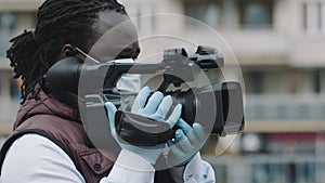 Close up, african black videographer with medikal mask looking through the viewfinder on video camera