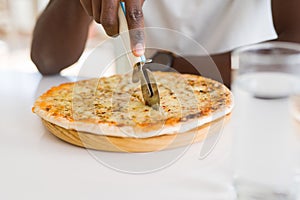 Close up of african man cutting a slice of cheese pizza using a cutter