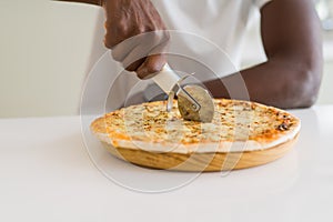 Close up of african man cutting a slice of cheese pizza using a cutter