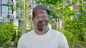 Close up African man looks camera on background building and trees in summer