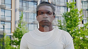 Close up African man looks camera on background building and trees in summer