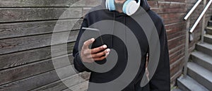 Close up african man with phone listening to music in headphones wearing a black hoodie on city street