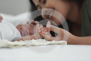 Close up of African new born baby holding mother`s finger while he is sleeping on bed. Young mom touch little infant boy`s head