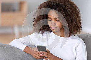 Close up african teenager girl sitting on couch using smartphone