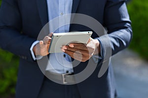 Close up of afro american businessman hands using tablet. A black business man in a formal suit browses the internet mobile device