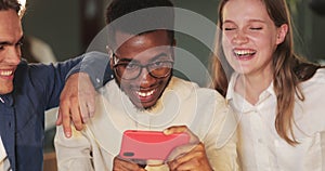 Close up of afro american guy holding phone and showing friends funny photo. Joyful young people laughing and looking at