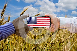 Close up of afroamerican and caucasian white hands holding the phone with US flag in front of a wheat field. America above all