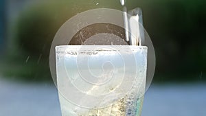 Close-up of Air bubble while pouring mineral carbonated water with ice into glass on green nature bokeh background.