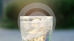 Close-up of Air bubble while pouring mineral carbonated water with ice into glass on green nature bokeh background.