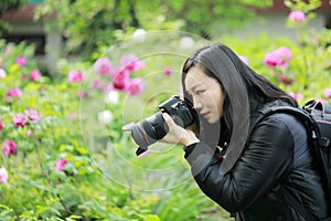 Close up Aisan Chinese woman photographer hold camera close to her face work in nature against blue sky