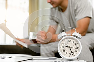 Close up Alarm clock on table with blurred man is working in background at home. Concept work at home