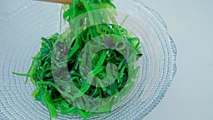 Close up of an algae with chopsticks. Soaked green wakame.