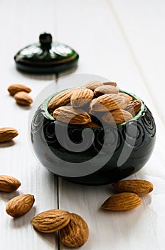 close-up, almonds in a green wooden bowl on a white wooden table