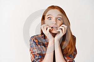 Close-up of amazed redhead girl listening with interesting, biting fingernails tempted and amused, looking at camera