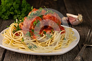 Close-up of American spaghetti with meatballs and tomato sauce with garlic and onions on a rustic wooden background