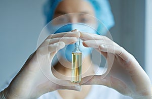 Close-up ampule with liquid drug in hands in gloves. doctor or scientist in laboratory blurred on background.