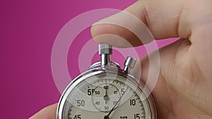 Close-up analog stopwatch in man`s hand on pink background is starting and stopping