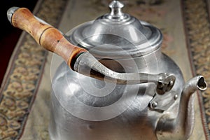 Close-up of ancient metallic teapot with wooden handle on an embroidered mat