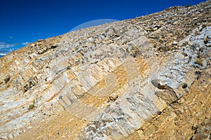 Close up of ancient sedimentary layered rock outcrop, folded by the power of geologic crustal movement. Clear blue sky.