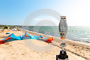 Close-up anemometer wind meter gadget against surf kite equipment on sand beach shore watersport spot on bright sunny