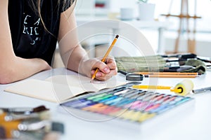 Close-up angle view of a female painter drawing draft at sketchbook using pencil. Artist sketching in art studio with