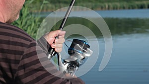 Close up angler holding carp fishing rod with reel at riverbank