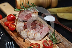 Close up Angus beef steak sliced with the black pepper, tomato, potato on the black wooden table. Foods concept