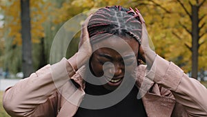 Close-up annoyed african american young woman standing outdoors covering ears with hands from loud noise feeling