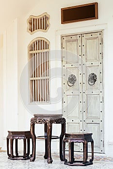Close up antique chinese traditional chairs and table with white Chino-Portuguese door background. Asia architecture vintage style