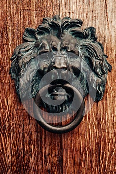 Close up of antique metal doorknob with lion head on brown wooden door. Old bronze traditional knocker.