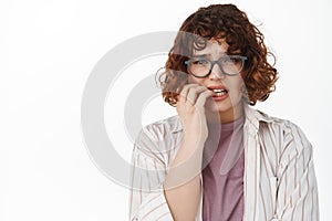 Close up of anxious and scared young woman in glasses, curly hair, biting fingernails and looking worried, feel nervous