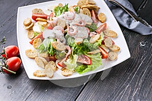 Close-up appetizing salad with shrimp, lettuce, cheese, avocado and crackers on a white plate. Delicious and healthy seafood