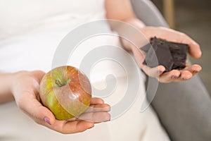 Close up apple and chocolate in pregnant woman hands