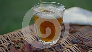 Close-up apple juice pouring in glass outdoors with dried fruits lying on picnic basket. Healthful organic vitamin drink