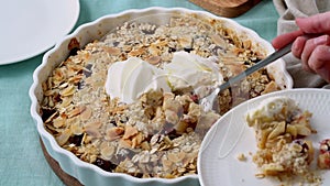 Close up apple pear crumble with ice cream, streusel. Woman putting pie on plate with spoon.