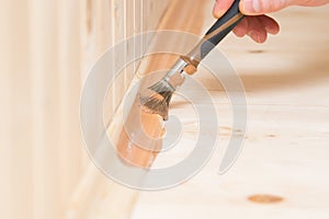 Close-up applying dark varnish on a wooden baseboard of an interior floor