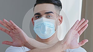 Close-up arabic ethnic man in medical protective mask shows stop gestures prohibits crossing arms hands, portrait male