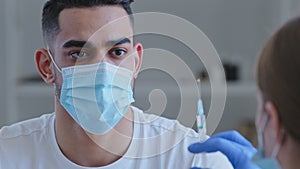 Close-up arabic spaniard man in medical mask sits in clinic hospital preparing for vaccination injection looks at