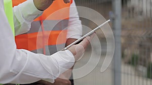 Close up of architect hands using tablet near construction site. The builder and architect man are discussing the